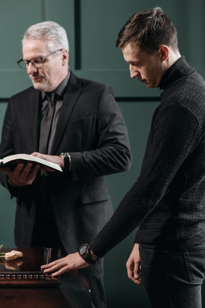 A Man Holding a Wooden Surface Standing Next to a Man Reading a Book